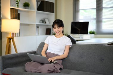 Oturma odasında dizüstü bilgisayarla rahatlayan genç bir kadın..