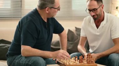 Yaşlı baba ve yetişkin oğul rahat oturma odasında satranç oynuyorlar. Babalar Günü konsepti