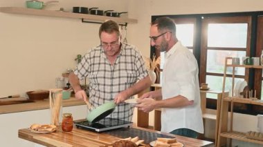 Gülümseyen baba ve yetişkin oğul sıcak bir ev mutfağında makarna hazırlıyorlar. Babalar Günü konsepti.