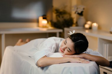 Masaj masasında mumlar ve yumuşak ışıklandırmayla rahatlayan genç bir kadın. Refah kavramı.