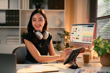 Neşeli grafik tasarımcısı ekranında renk paletleri olan yaratıcı bir stüdyoda dijital tablet üzerinde çalışıyor..