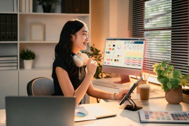 Renk çizelgeleri ve tasarım araçlarıyla dolu modern bir çalışma alanında dijital tablet kullanan kadın grafik tasarımcısı.