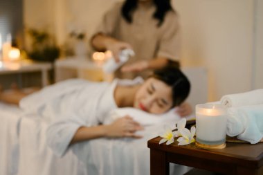 Aromaterapi mumu ve ön planda havlular, masaj masasında bayan müşteriyle...