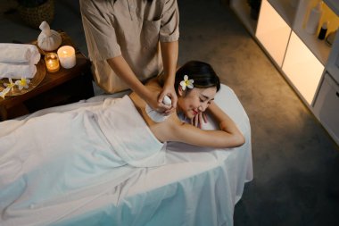 Huzurlu bir spa seansı, sağlık merkezindeki gülümseyen bir bayan müşteriye bitkisel kompres terapisi gösteriyor..