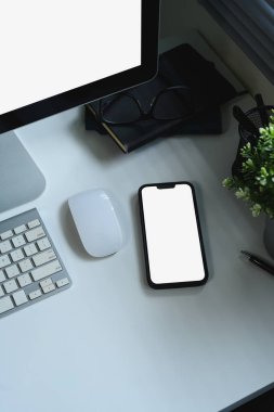 Modern beyaz masa çalışma alanı üzerinde boş ekranlı akıllı telefonun üst görünümü.
