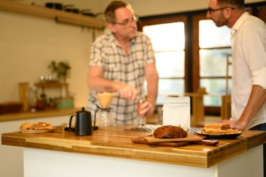 Ahşap tezgah, kahve aletleri, taze ekmek ve arka planda baba-oğul. Babalar Günü konsepti.