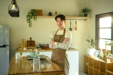 Önlük takan, elinde kaşıkla ev mutfağında duran kendinden emin genç bir adam..