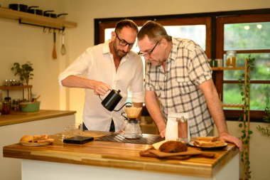 Son sınıf öğrencisiyle oğlu sıcak bir mutfakta kahvelerini yudumluyorlar. Babalar Günü konsepti.