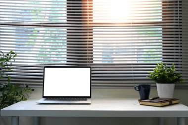 Laptop, defter ve küçük bitkilerle beyaz bir masanın üzerinde modern minimalist ofis düzeni..