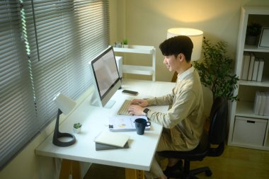 Modern bir ev ofisinde masaüstü bilgisayarı üzerinde çalışan odaklanmış girişimci..