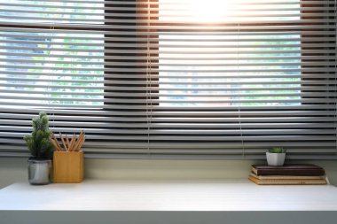 Panjurlardan geçen kitaplar, kalemler ve güneş ışığıyla minimalist ev çalışma alanı.