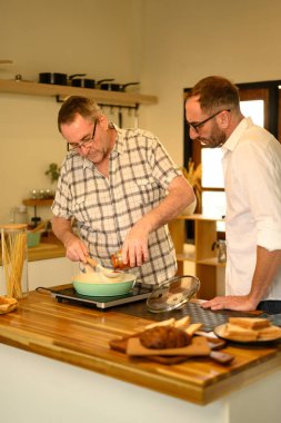 Mutlu kıdemli adam ve oğlu mutfakta ev yemeği hazırlarken eğleniyorlar. Babalar Günü konsepti.