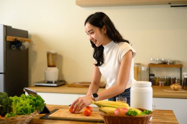 Genç bir kadın domates doğruyor ve yemek pişirme talimatları için dijital tablet kullanıyor..