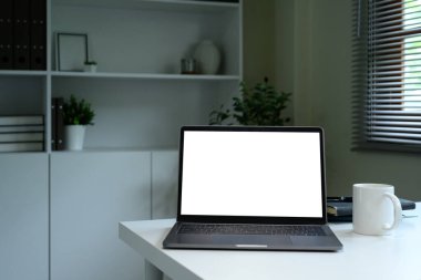 Boş dizüstü bilgisayarı, kahve fincanı ve beyaz masasında kitapları olan modern çalışma alanı..