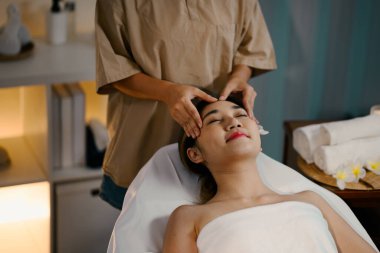 Genç kadın spa 'da kafa masajı yaptırıyor, gözleri kapalı ve huzurlu bir ifade sergiliyor..