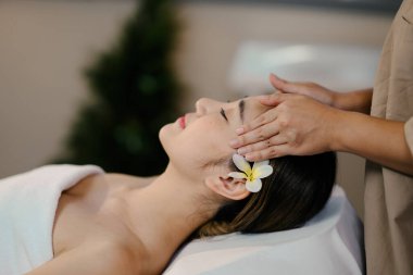 Sakin bir kaplıcada gözleri kapalı, rahatlatıcı bir kafa masajının keyfini çıkaran genç bir kadın..