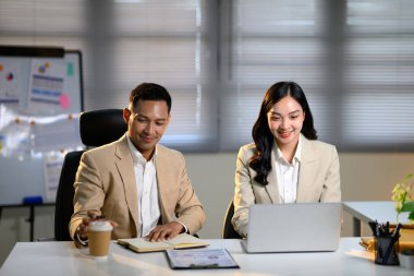 Masasında dijital aletler olan bir projede çalışan gülümseyen meslektaşlar..