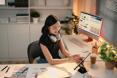 Renk paletleri olan yaratıcı bir ofiste dijital tablet kullanarak gülümseyen genç grafik tasarımcısı.