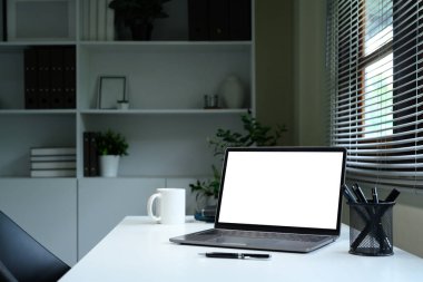 Boş dizüstü bilgisayarı, kahve fincanı ve pencere kenarında kalem tutacağı olan modern ofis masası..