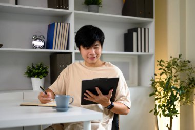 Genç adam bir panoya gönderme yaparken notlar yazıyor, evden çalışıyor..