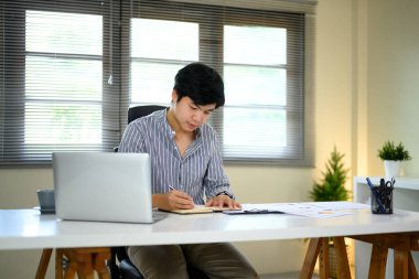 Adam parlak ve modern bir çalışma alanında dizüstü bilgisayar planlamaya ya da günlük tutmaya odaklanmış..