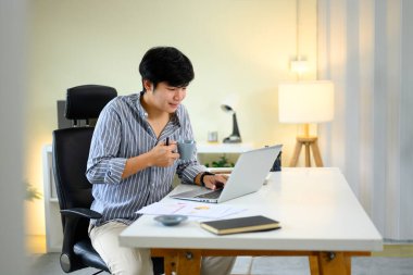 Uzaktan kumandalı rahat bir işçi verimli bir online çalışma sırasında sıcak bir içkinin tadını çıkarıyor..