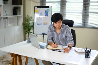 Evinde çalışan, belgeleri inceleyen ve ofiste notlar alan genç bir adam..