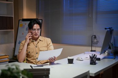 Ofiste geç saatlere kadar çalışan bir iş adamı, gece işi sırasında akıllı bir telefonla konuşuyor..