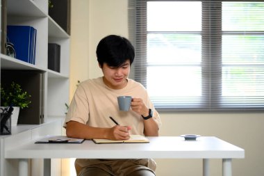 Genç adam sabah kahvesinin keyfini çıkarırken ofisteki not defterine notlar yazıyormuş..