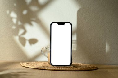 Boş ekranın ön görüntüsü ahşap masanın üzerindeki kahve fincanı ve sıcak güneş ışığı gölgeleri..