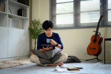 Genç adam çarmıhta oturmuş yerde yumurta atıyor, kahve içiyor ve evde tablet okuyor..