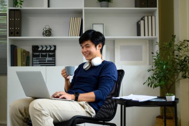 Rahat erkek serbest çalışan evde bilgisayarını kullanırken sıcak içkinin tadını çıkarıyor..