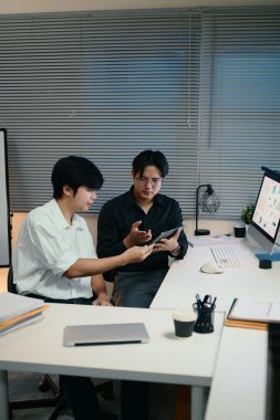 Geceleri modern bir ofiste dijital tablet verilerini inceleyen iki işadamı..