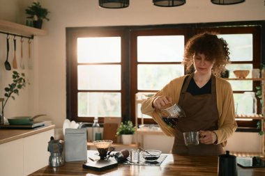 Genç bir kadın parlak bir mutfakta bir fincan taze filtre kahve hazırlıyor..