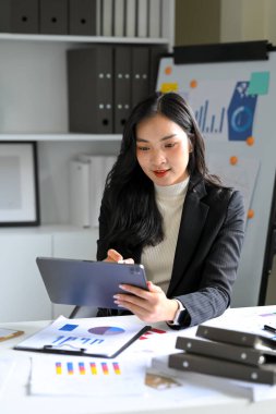 İş kadını, masasındaki dijital tablette mali tabletleri ve grafikleri analiz ediyor..