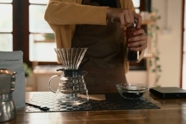 Genç bir kadın ahşap tezgahta elle öğütücü kullanarak damlatılmış kahve yapmaya hazırlanıyor..