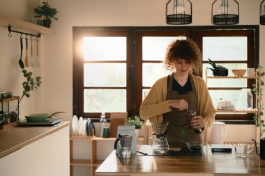 Genç bir kadın ahşap tezgahta elle öğütücü kullanarak damlatılmış kahve yapmaya hazırlanıyor..