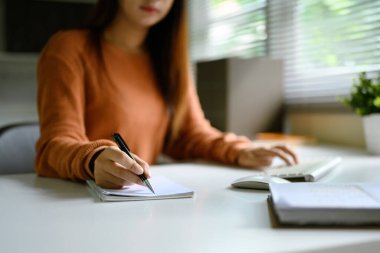 Ofis malzemeleriyle birlikte minimalist beyaz bir masada oturan odaklanmış bir kadın..