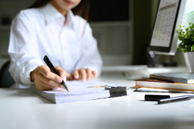 Beyaz gömlekli bir iş kadını modern bir masadaki basılı iş raporlarını inceliyor..