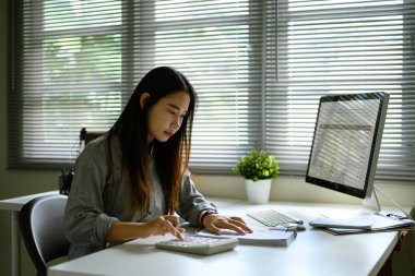Hesap makinesi kullanan ve masasındaki mali raporları inceleyen bir kadın..