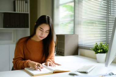 Ofis malzemeleriyle birlikte minimalist beyaz bir masada oturan odaklanmış bir kadın..