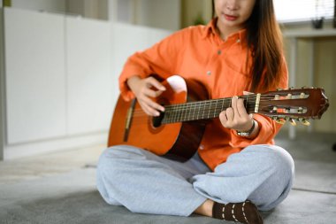 Kapalı alanda gitar çalan Asyalı bir kadın. Panjurlardan içeri ışık süzülüyor..