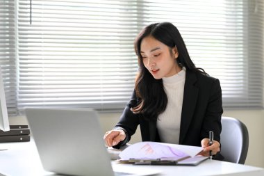 Modern bir ofisteki masasında belgeleri inceleyen odaklanmış bir iş kadını..