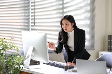 Parlak bir ofiste çalışırken bilgisayar ekranındaki verileri analiz eden odaklanmış iş kadını.