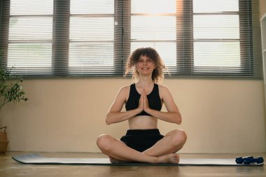 Evde yoga yapan genç bir kadın. Nilüfer pozisyonunda oturmuş dua ediyor..