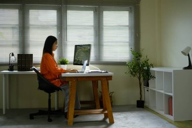 Parlak bir ev ofisinde muhasebe işleriyle uğraşan bir kadının yan görüntüsü.