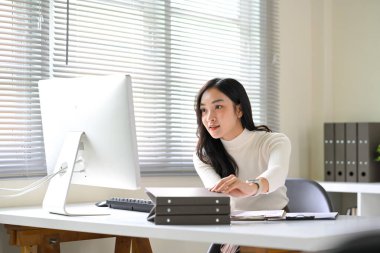 Parlak, modern bir ofis masasında masaüstü bilgisayarı üzerinde çalışan odaklanmış bir kadın..