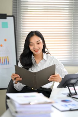 Asyalı ofis çalışanı iş yerindeki belgeleri inceliyor..