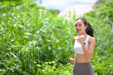 Zinde Asyalı kadın, parlak doğal ışık altında yemyeşil alanda koşuyor..