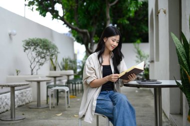 Rahat genç bir kadın açık bir kafede kitap okuyor..